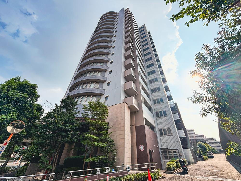 アルテヴィータ B棟 緑豊かな街並みに調和する、優美な曲線が印象的なランドマークレジデンス。気品ある佇まいが、住まう方のステータスを物語ります。青空に映える美しい外観です。